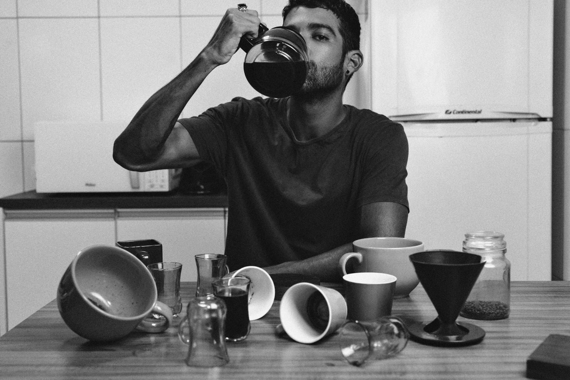 Man surrounded by empty coffee cups drinking from a coffee pot